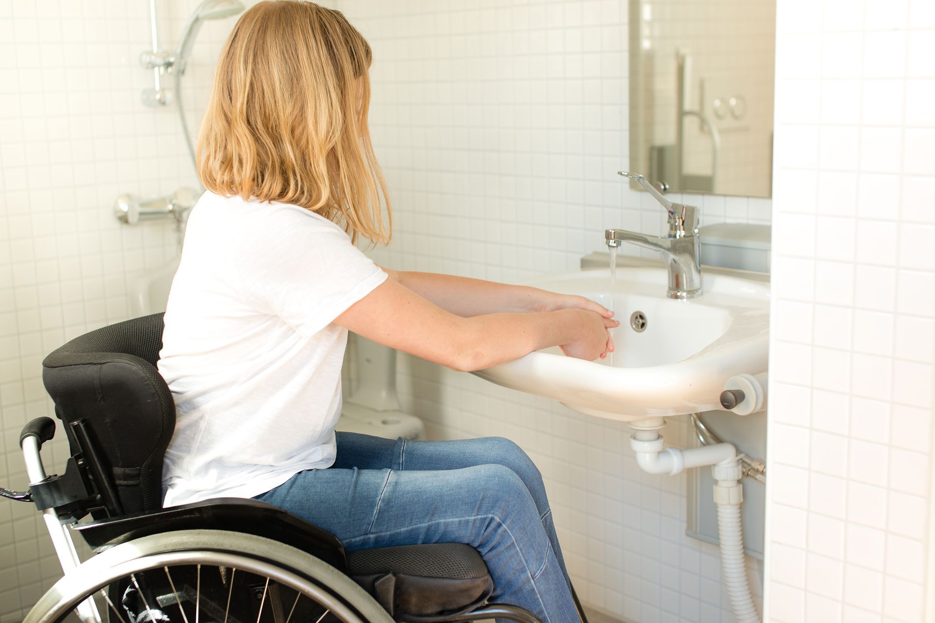 Woman in wheelchair washing hands at an accessible sink in a bathroom.