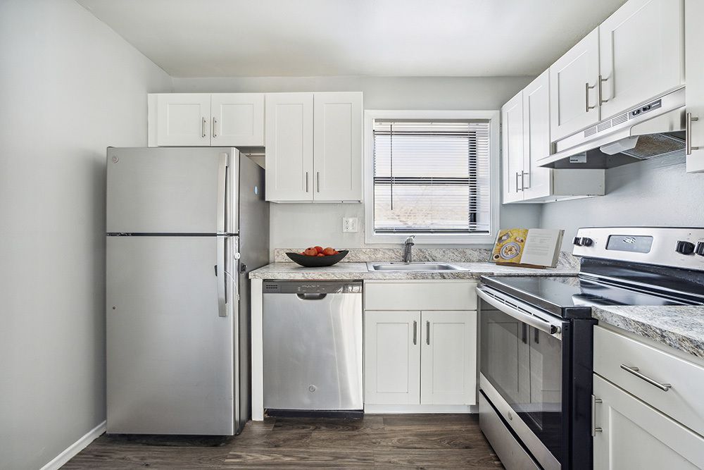 A small, white kitchen with stainless steel appliances, granite countertops, and a window.