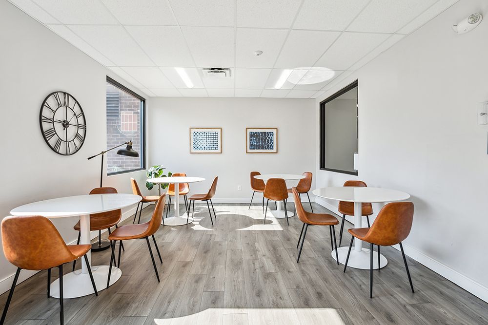 Cafe with white round tables, brown chairs, and artwork on light walls.