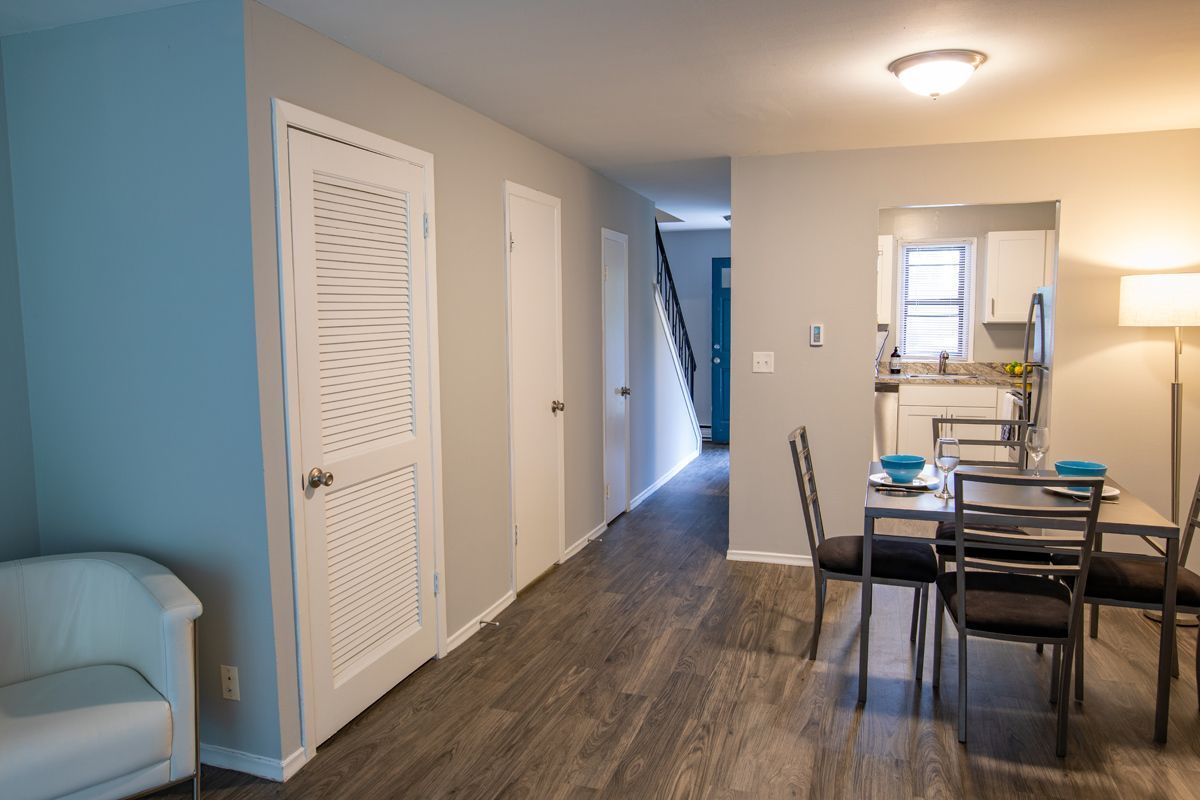 Interior view of dining area leading to hallway and kitchen; grey walls, wood-look floor, modern furniture.