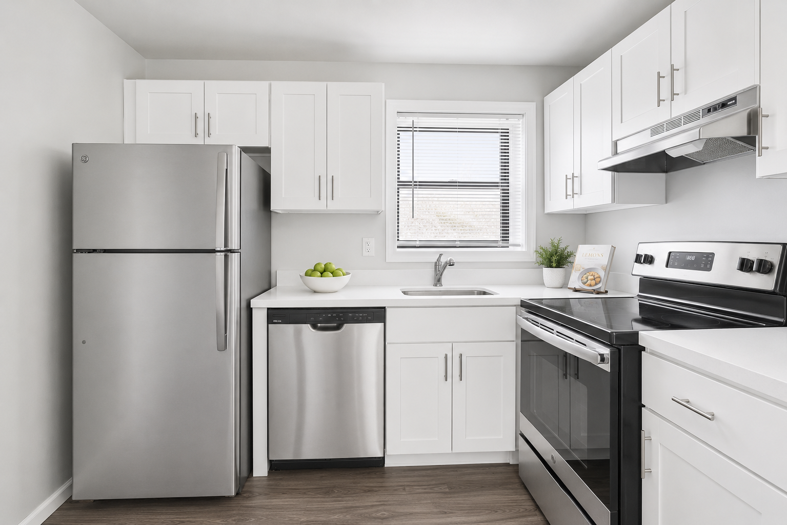 A small, white kitchen with stainless steel appliances, granite countertops, and a window.