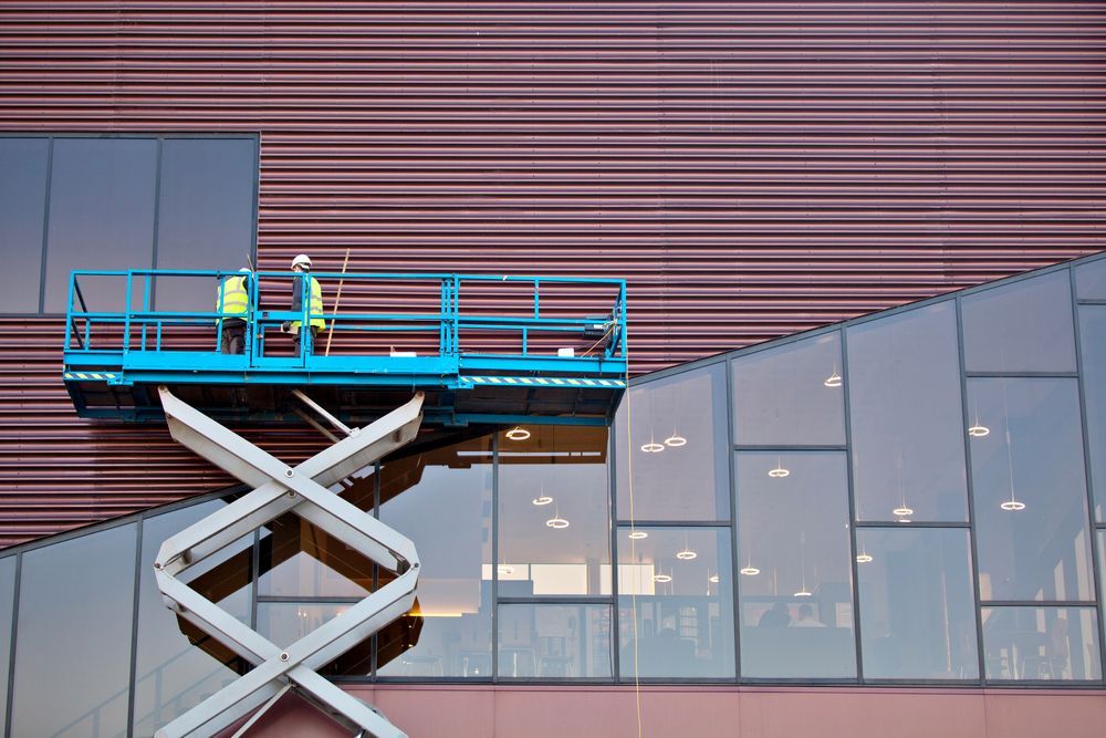 A Man is Standing on a Scissor Lift in Front of a Building — MPE Adventure Quads & Bikes In Muswellbrook, NSW