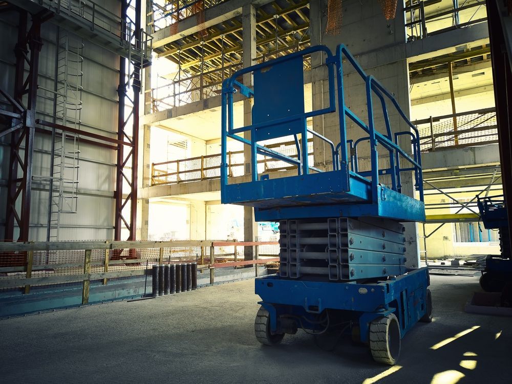 A Blue Scissor Lift is Parked in Front of a Building Under Construction — MPE Adventure Quads & Bikes In Port Stephens, NSW