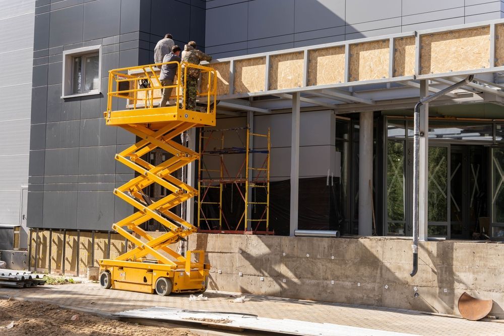 A Man is Standing on a Scissor Lift in Front of a Building — MPE Adventure Quads & Bikes In Lake Macquarie, NSW