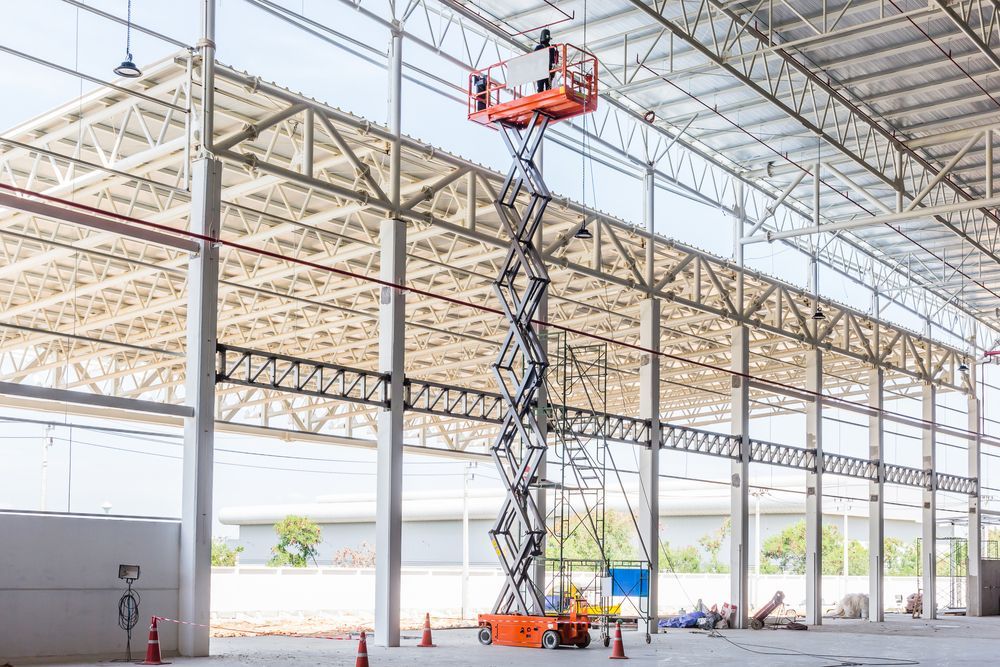 A Man is Standing on a Scissor Lift in a Large Warehouse — MPE Adventure Quads & Bikes In Gloucester, NSW