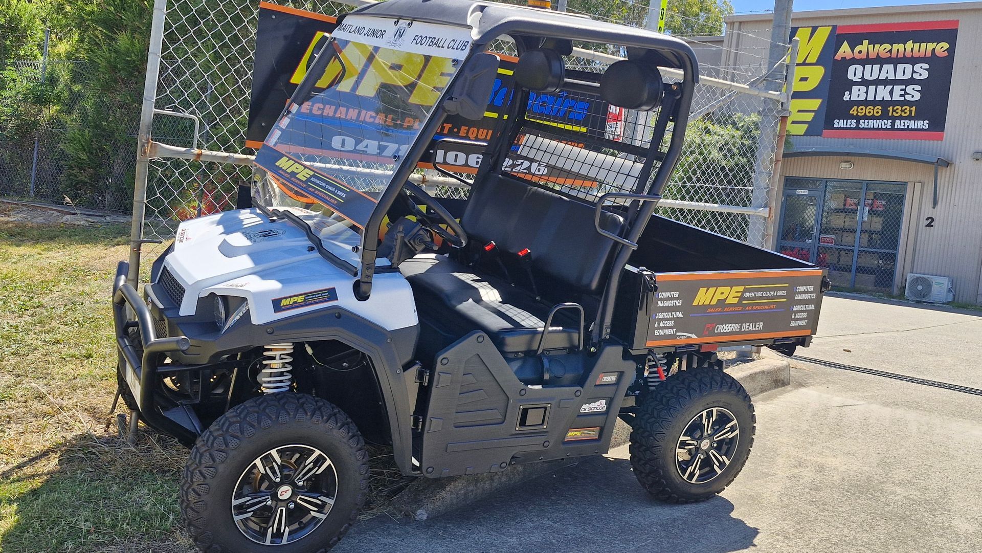 A white and black atv with the hood up is parked in front of a building — MPE Adventure Quads & Bikes In Thornton, NSW
