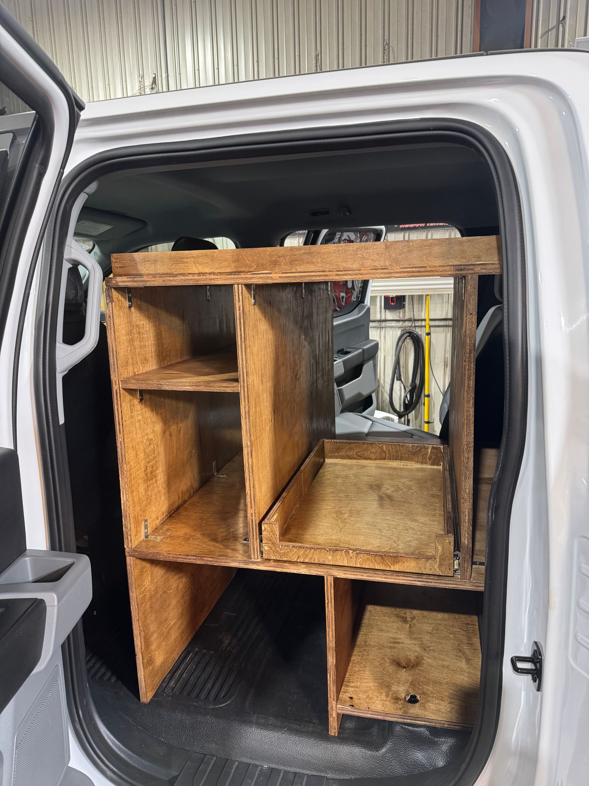 Wooden storage unit built inside a white vehicle, with shelves and compartments.