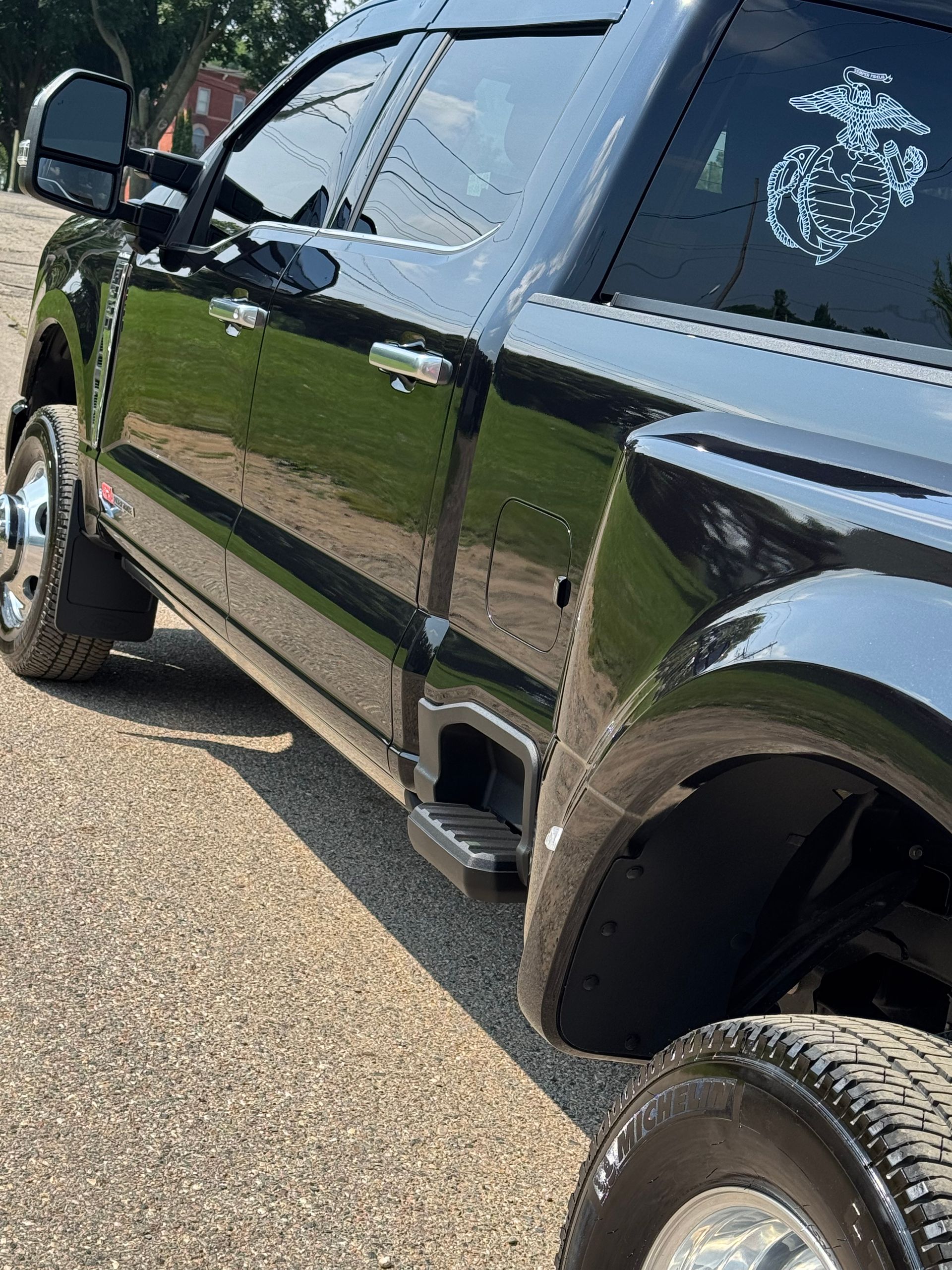 Black dually truck parked on pavement, side view. Has tinted windows and a Marine emblem.