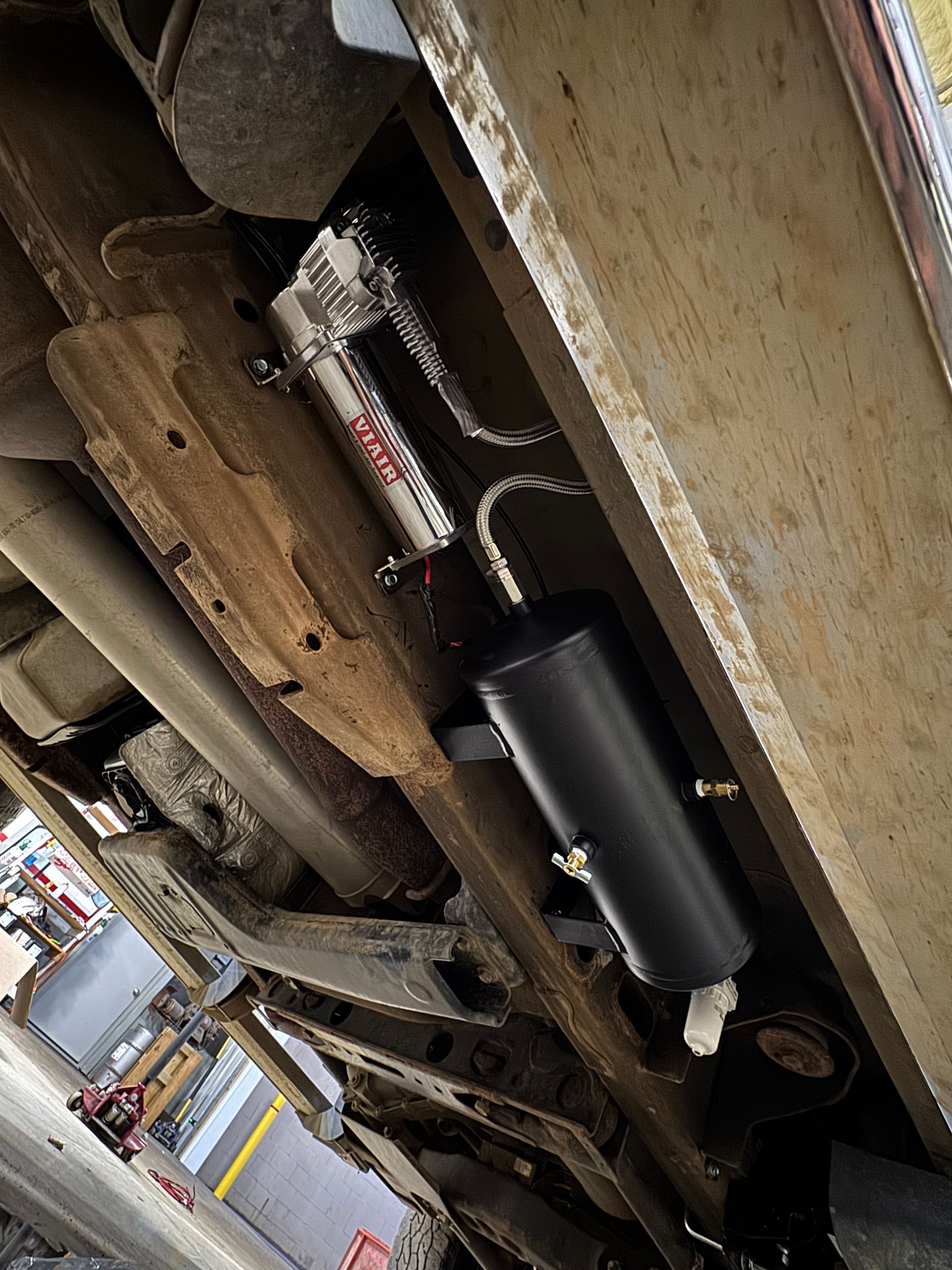 Undercarriage view with air compressor and tank mounted on a vehicle frame, black and silver components.