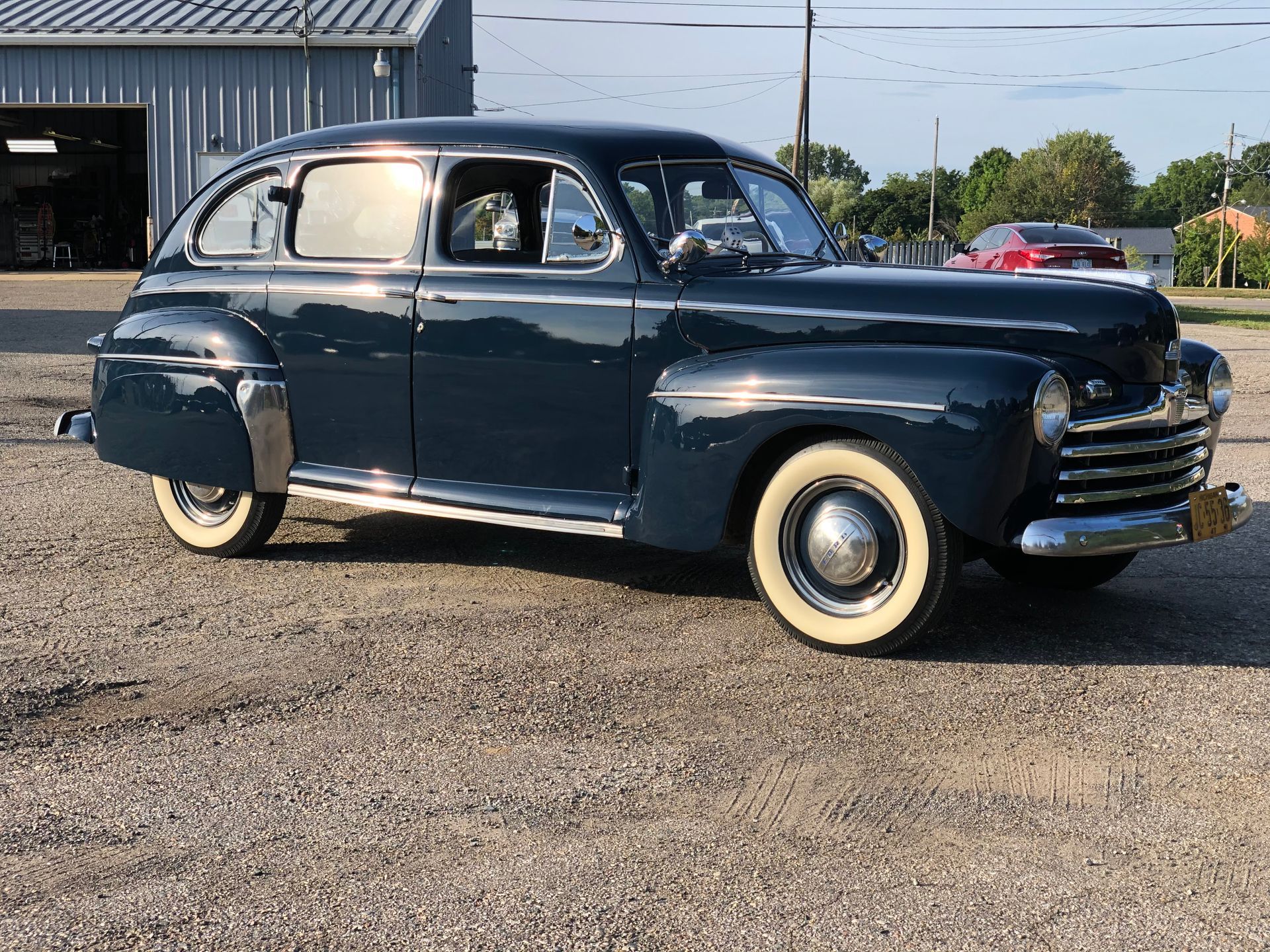 Dark blue vintage Ford car with whitewall tires parked on gravel.