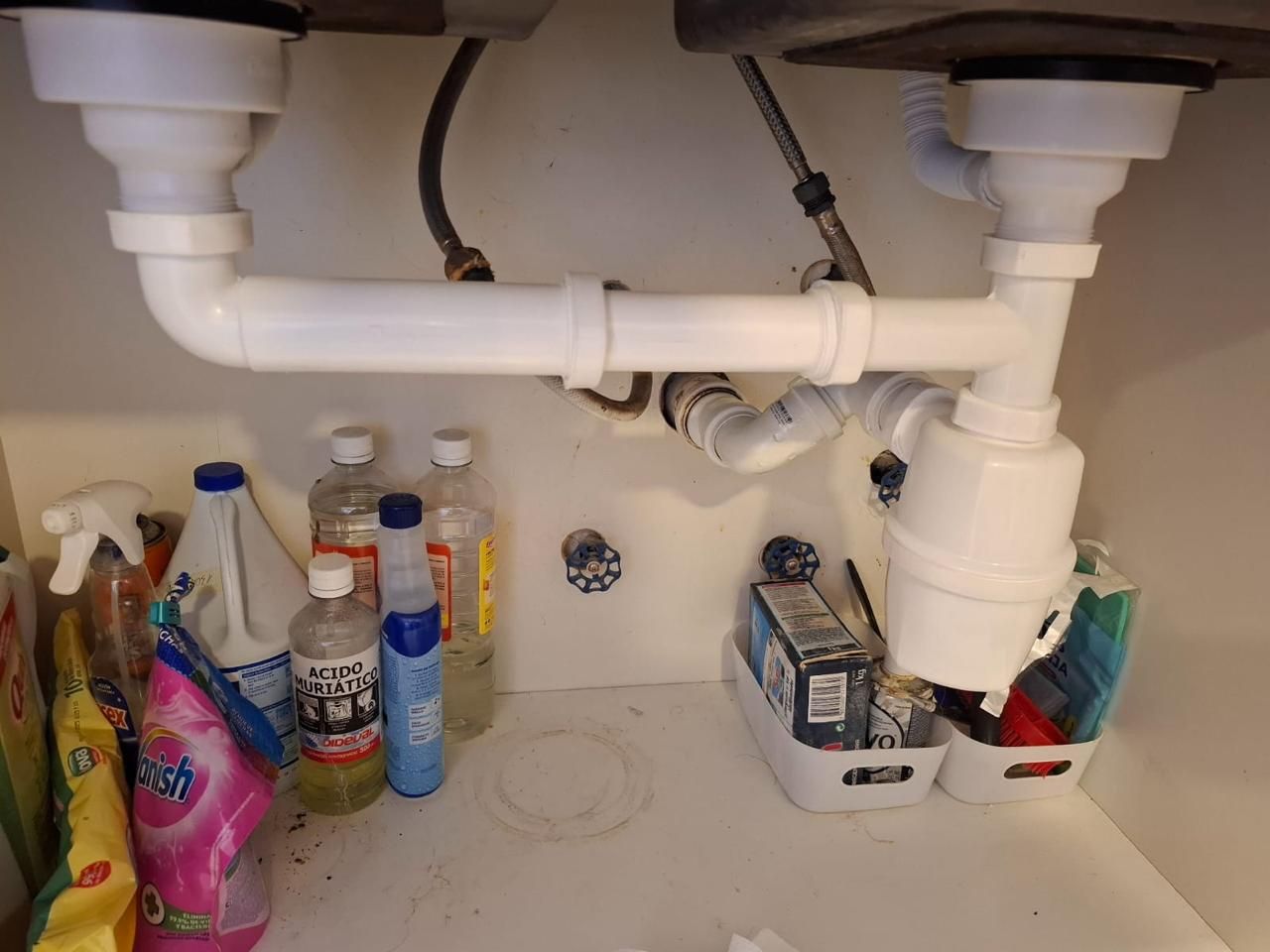 Instalación de tuberías debajo del fregadero: tuberías blancas, sifón y diversos productos de limpieza dentro de un armario.