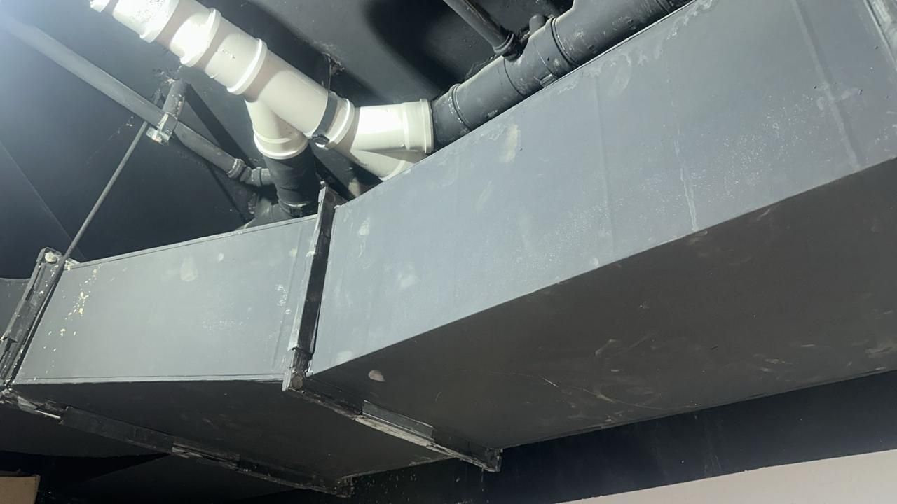 Conductos HVAC grises sobre un techo negro con tuberías de PVC blancas.