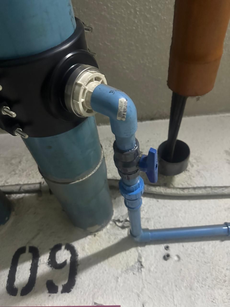 Instalación de plomería de PVC azul con válvula y codo contra una pared blanca; número 