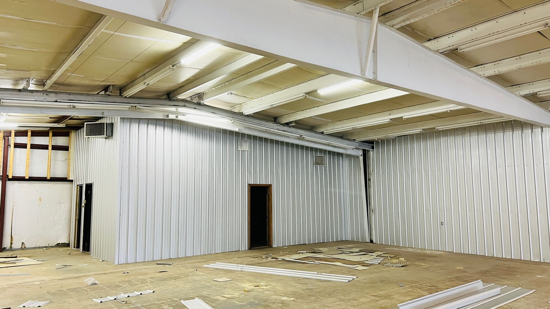 Interior of a building under construction, featuring corrugated metal walls, exposed beams, and a small doorway.
