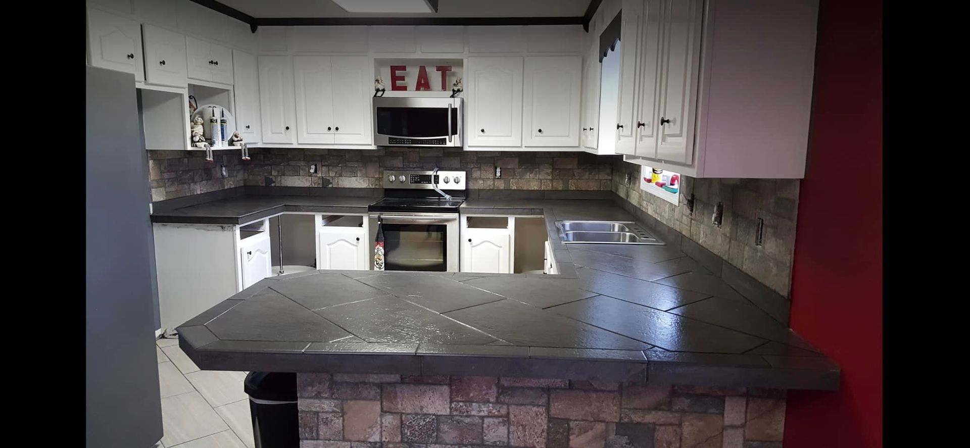 Kitchen with white cabinets, dark countertops, and stone-covered bar. Includes microwave and oven.