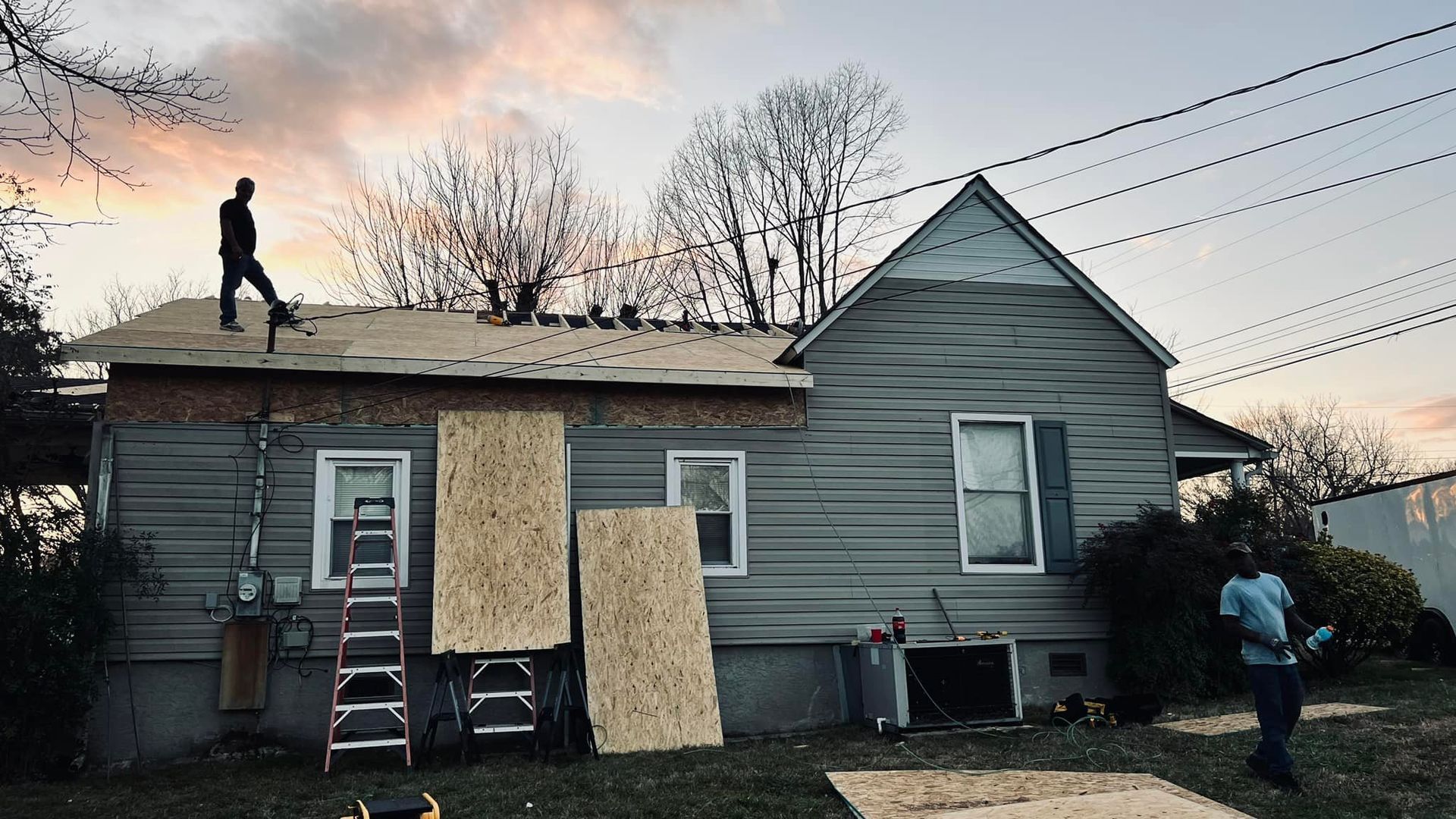 View from a rooftop: dark asphalt shingle roof, treeline in the background, blue sky.