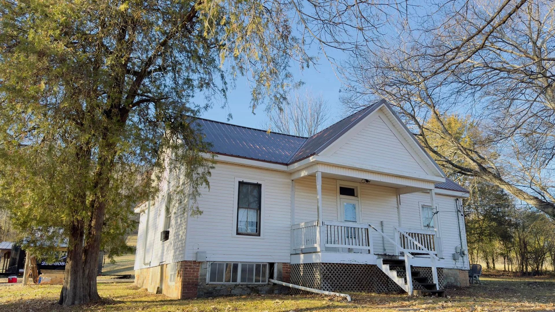 View from a rooftop: dark asphalt shingle roof, treeline in the background, blue sky.
