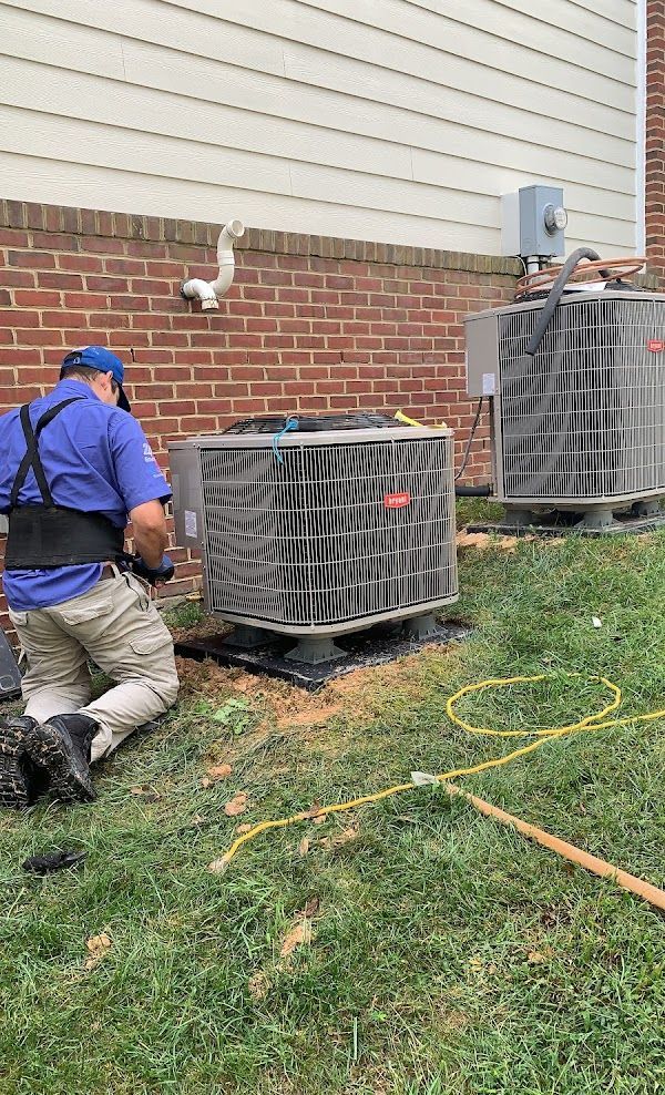 Alex HVAC Service LLC | HVAC technician kneels beside an air conditioning unit outside a brick building.