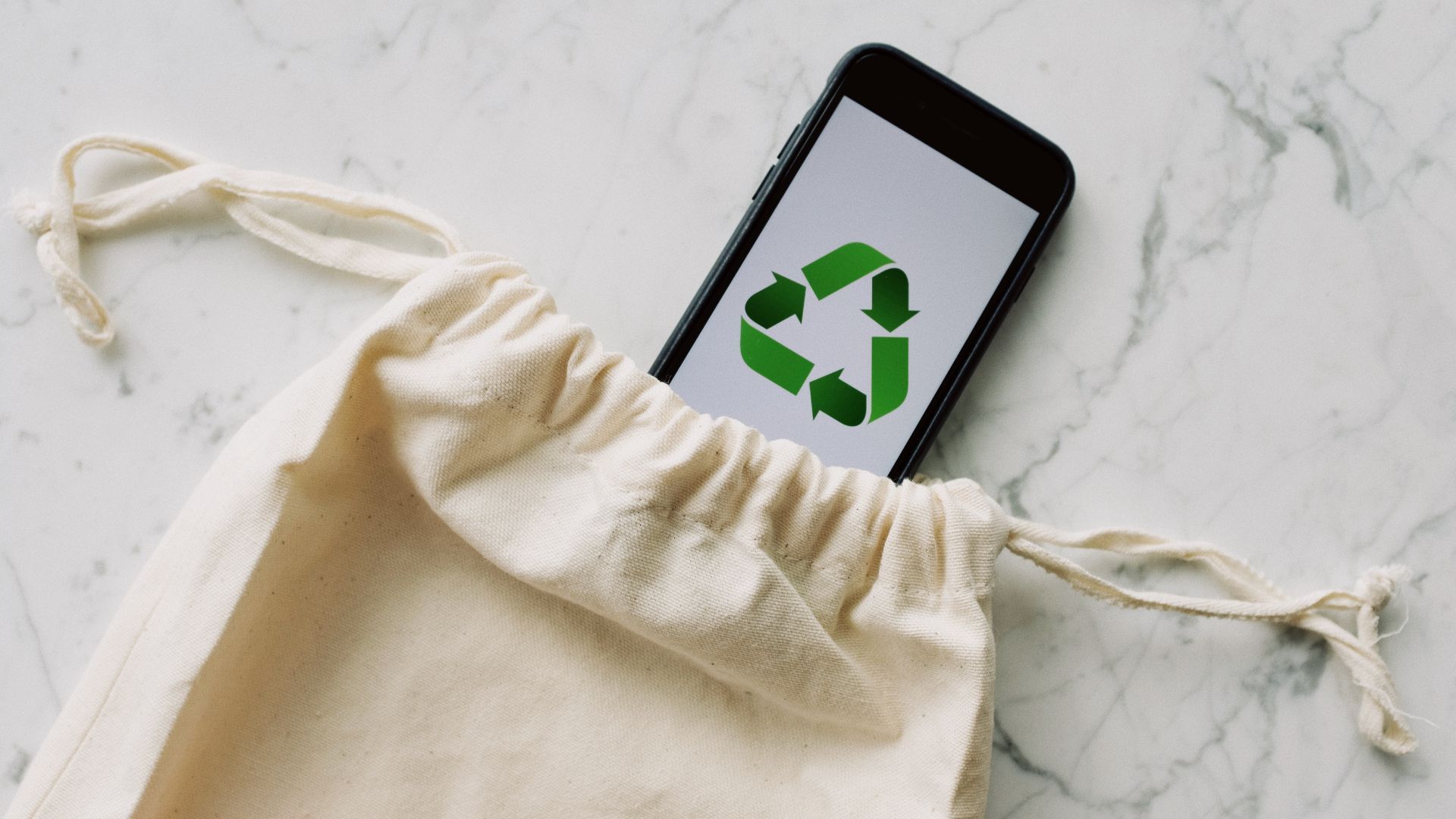 A cell phone with a recycling symbol on the screen is in a cotton bag.