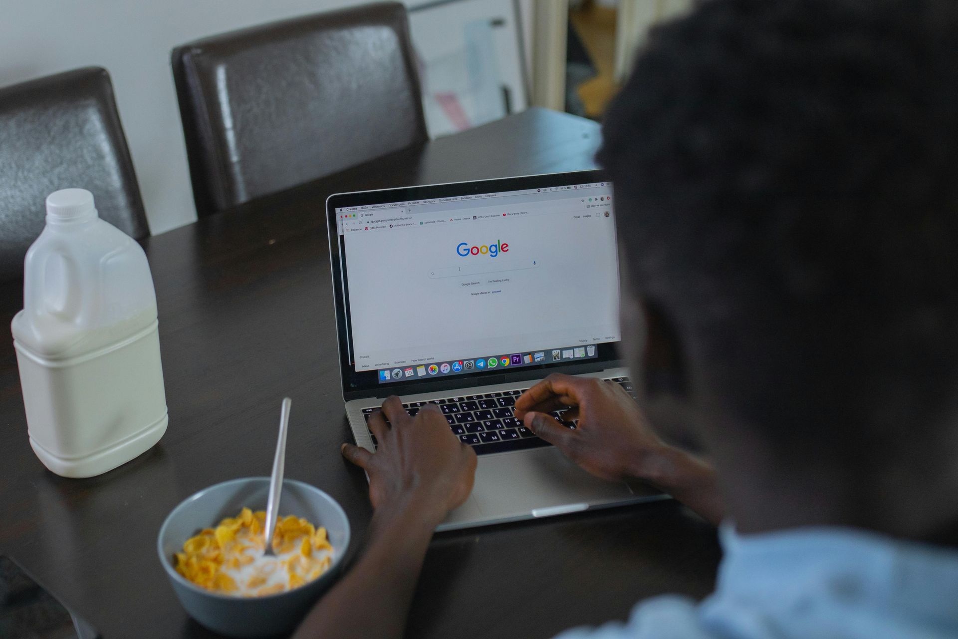 A person is typing on a laptop next to a bowl of cereal.