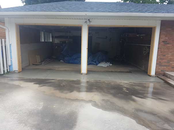 A garage with two doors open and a blue tarp on the floor.