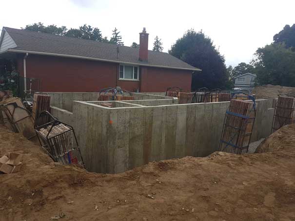 A large concrete wall is being built in front of a brick house.