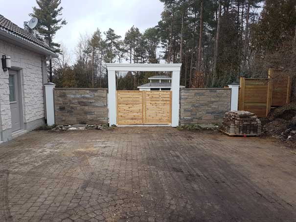 There is a wooden gate in the middle of a driveway.