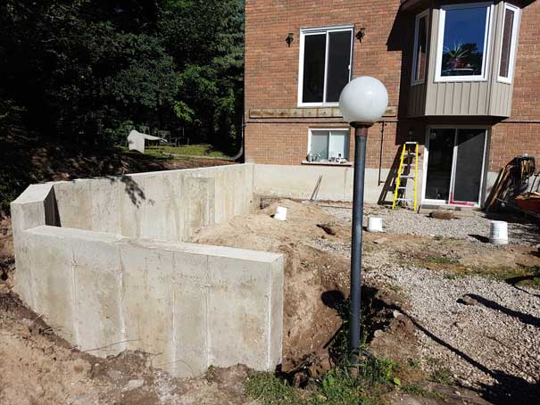 A large concrete wall is being built in front of a brick house.
