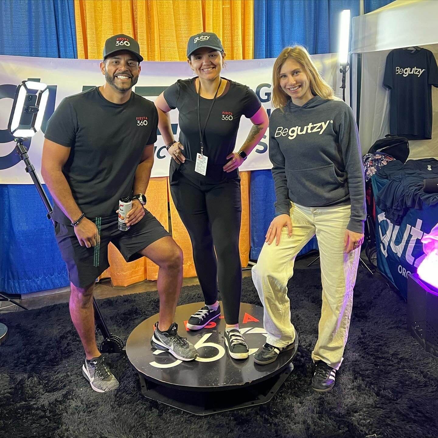 A man and two women are standing next to each other on a 360 degree photo booth.