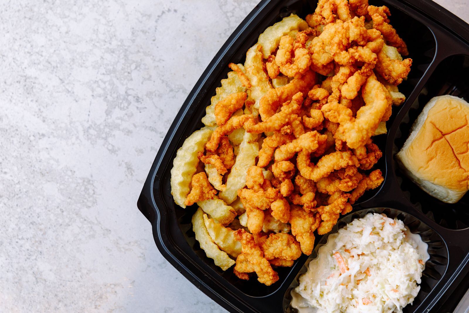 A plastic container filled with fried shrimp , french fries , and coleslaw.
