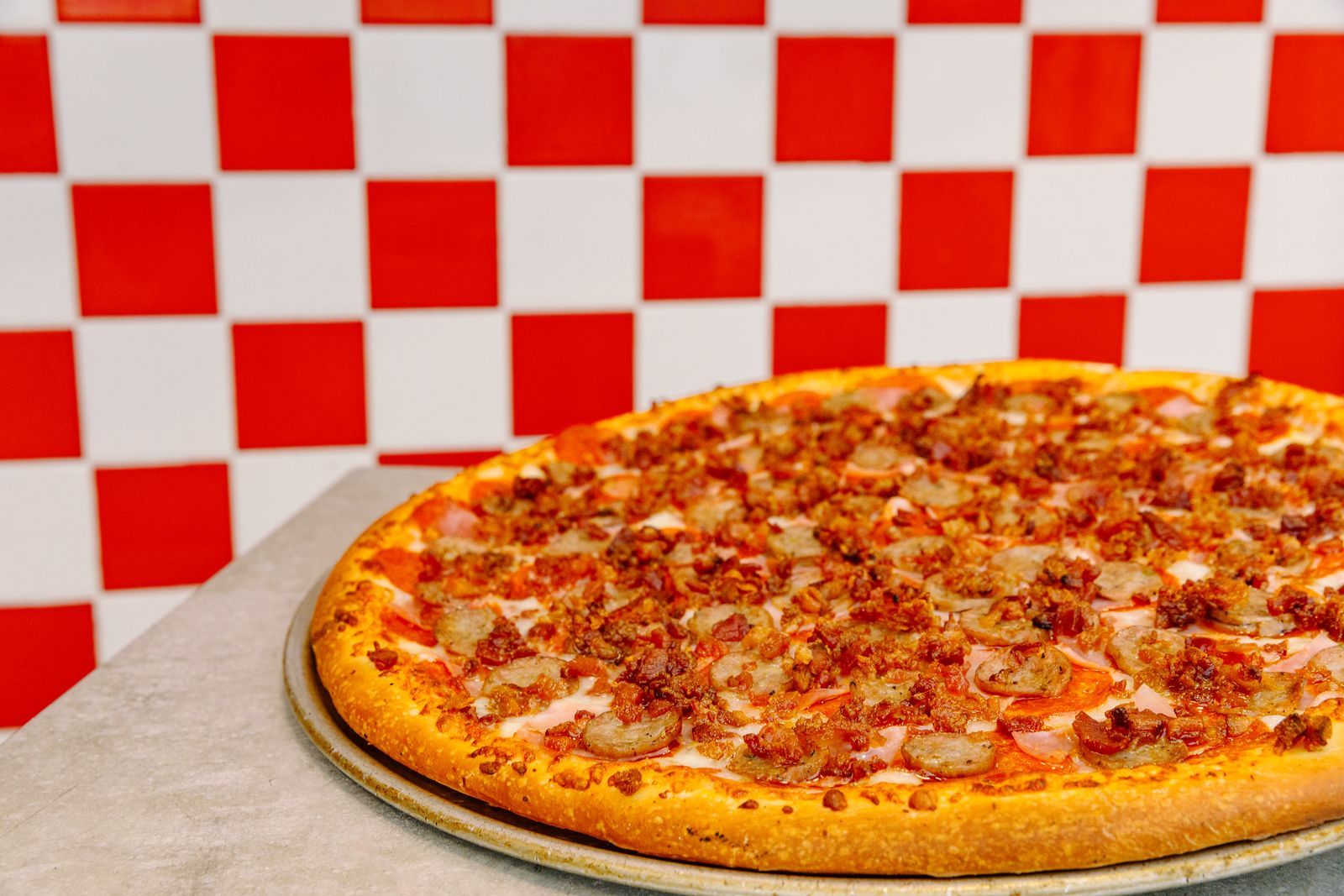 A pizza is sitting on a table in front of a checkered wall.