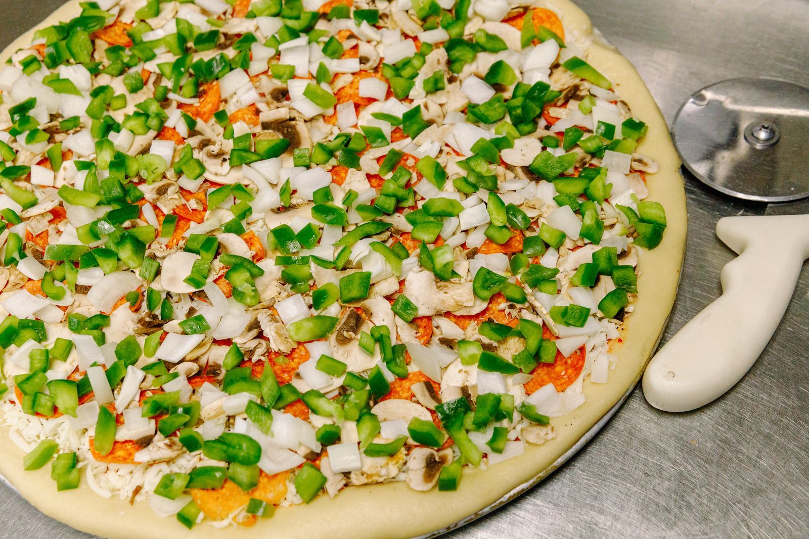 A pizza with mushrooms , peppers , onions and cheese next to a pizza cutter.