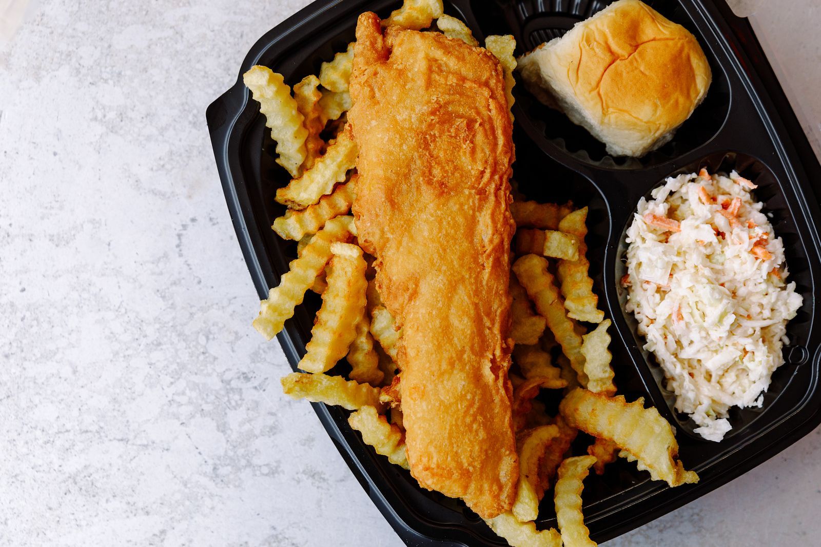 A plastic container filled with fried fish , french fries , coleslaw and a biscuit.