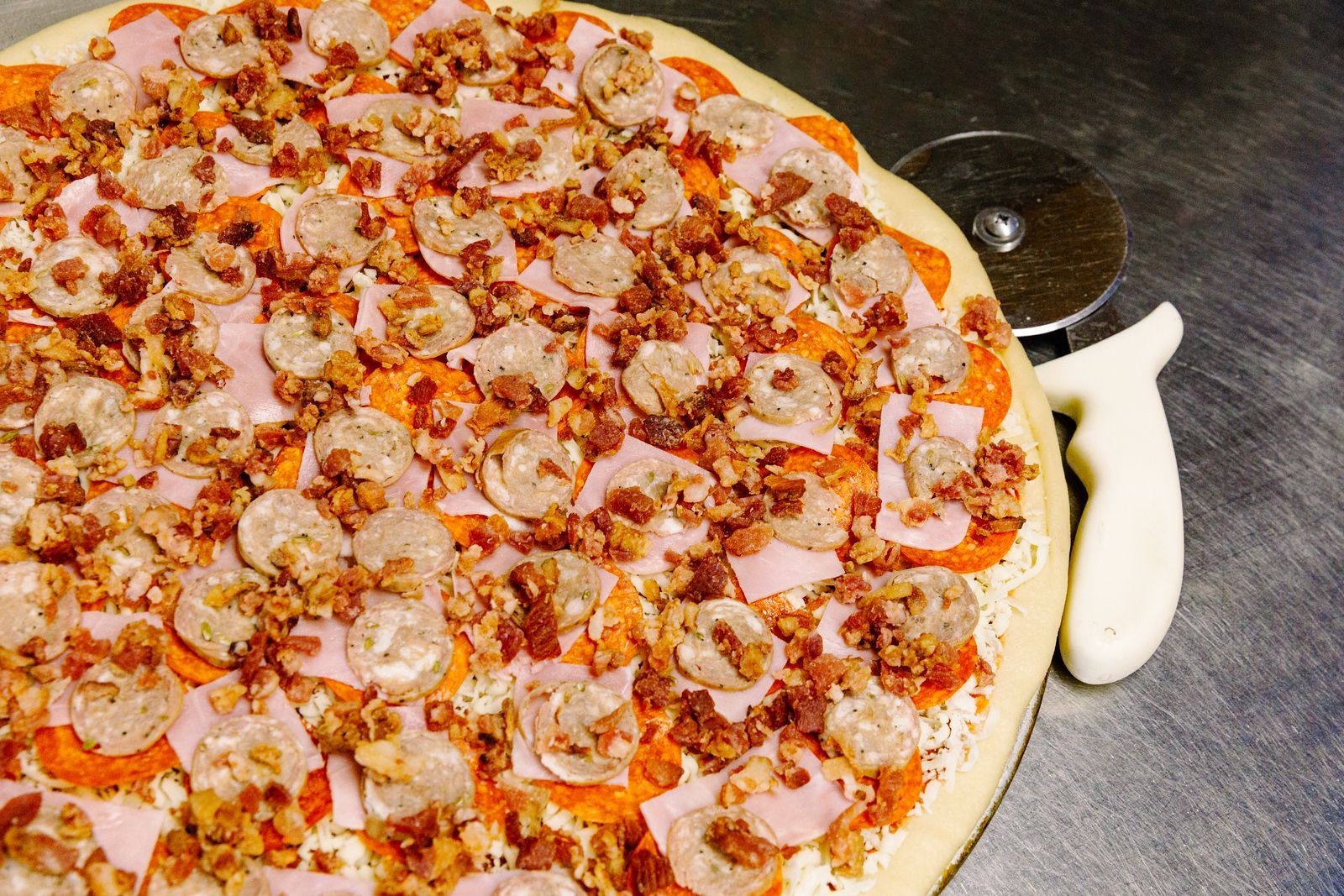 A pizza is sitting on a table next to a pizza cutter.