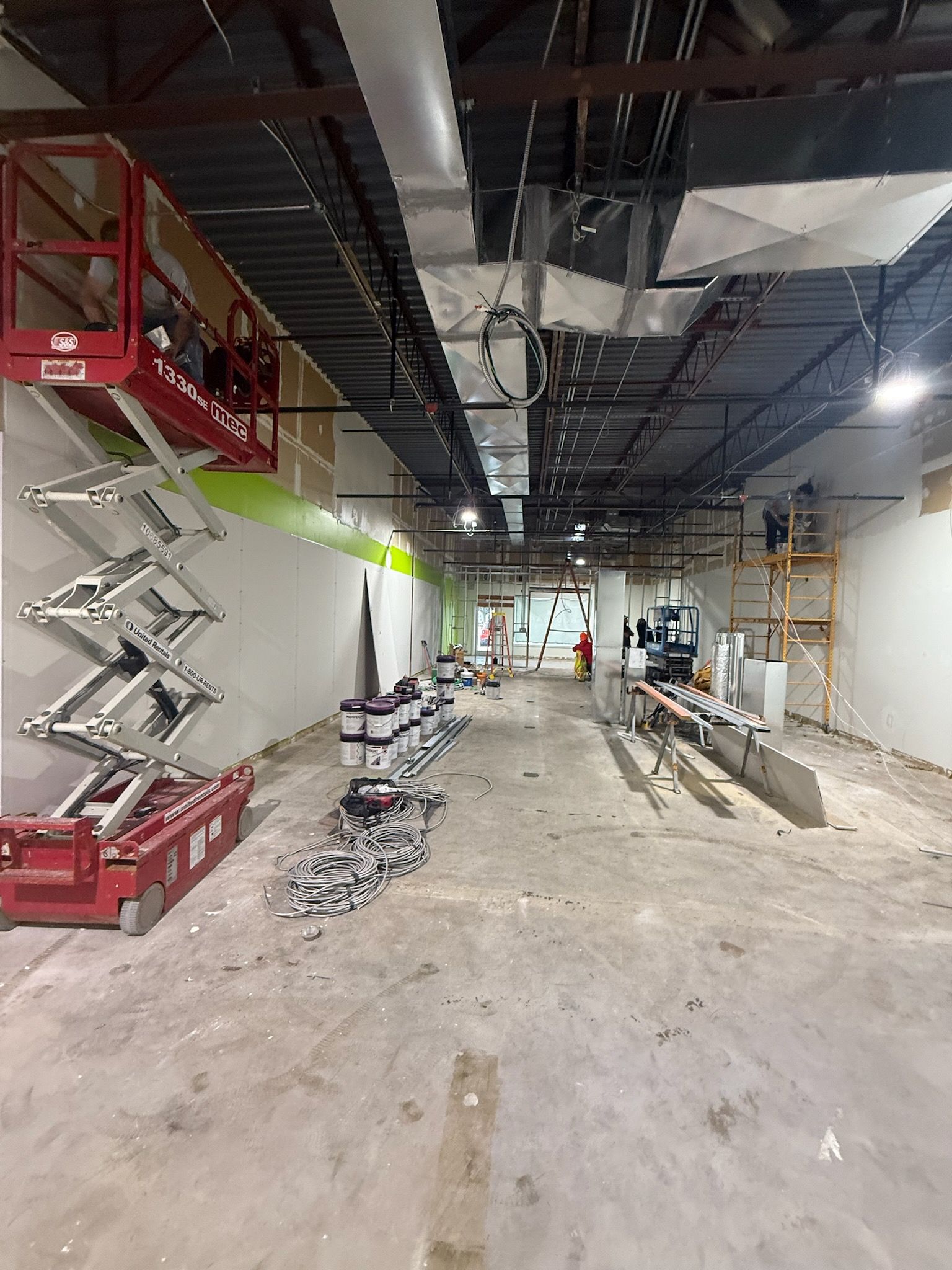 Construction site with scissor lift, exposed ceiling, and debris on the floor.