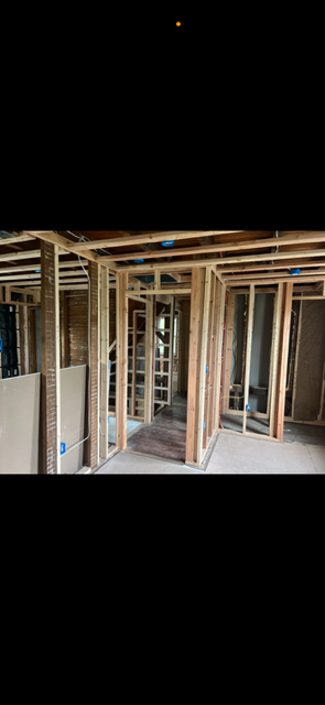 Interior of a house under construction; wooden framing, concrete floor, empty room, natural light.