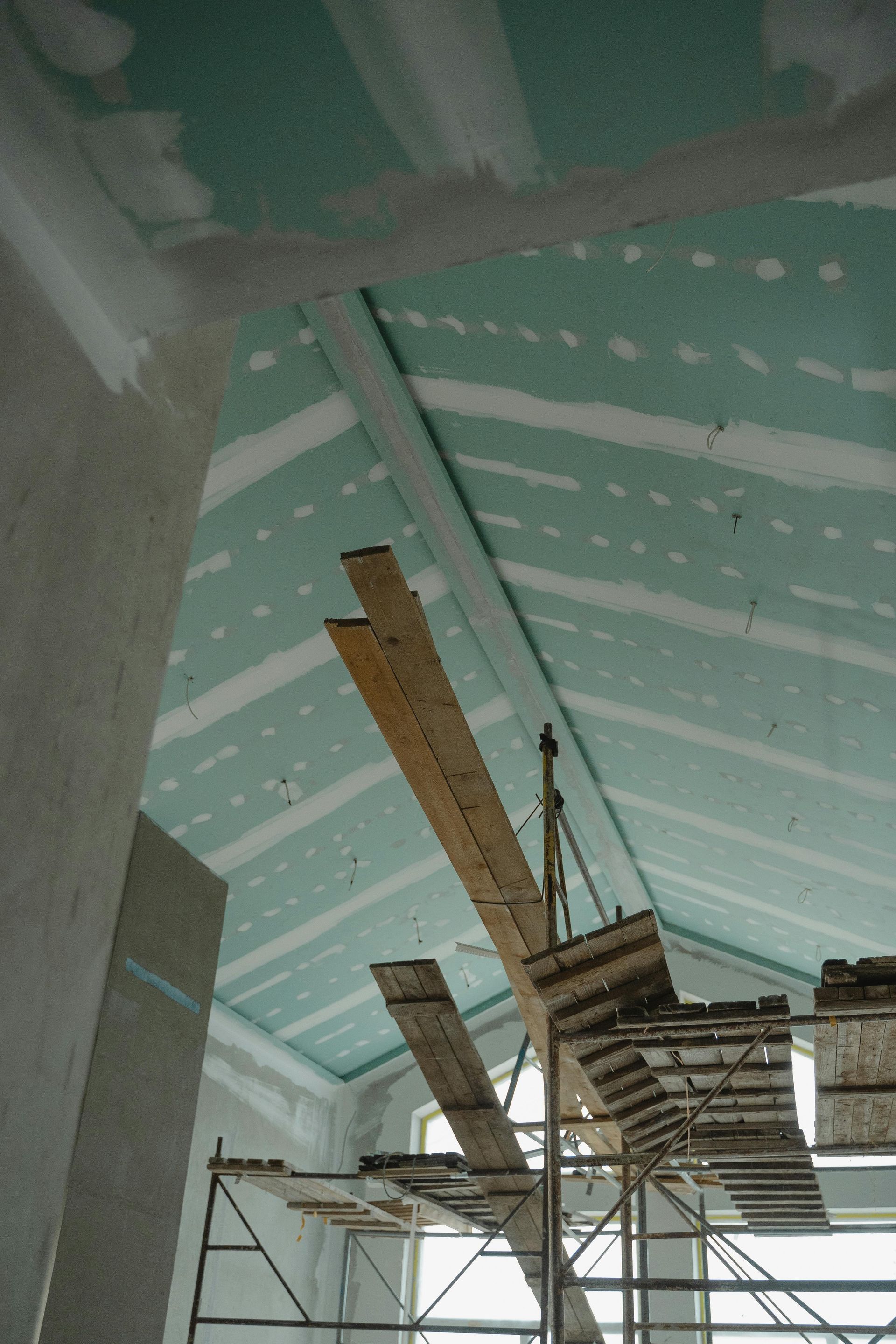 Interior construction site with green ceiling panels, scaffolding, and wooden planks overhead