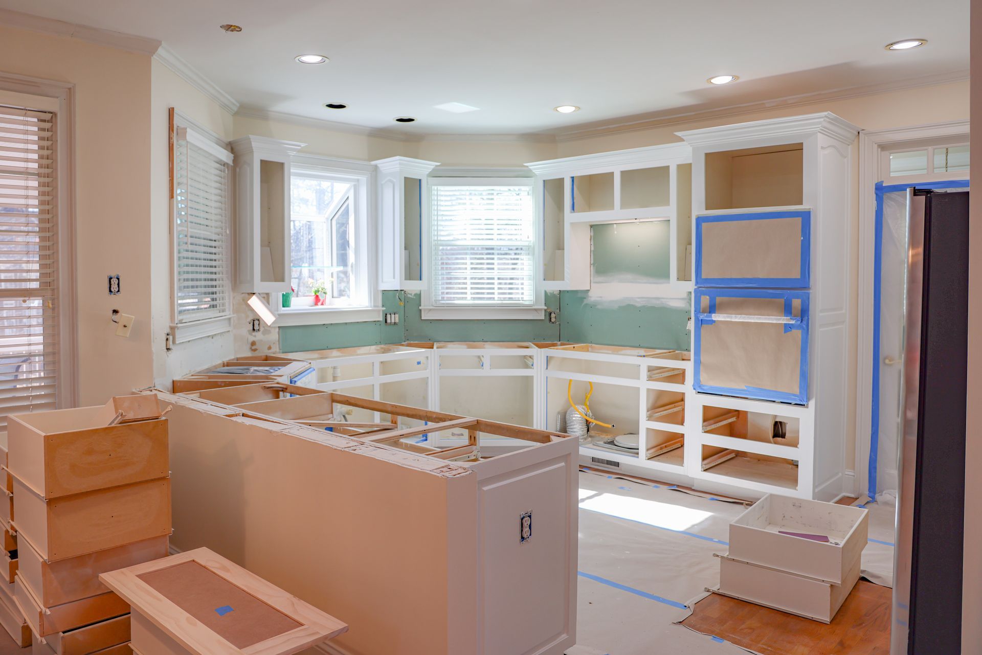 Kitchen renovation with unfinished white cabinets and drywall, construction materials, and sunlight.