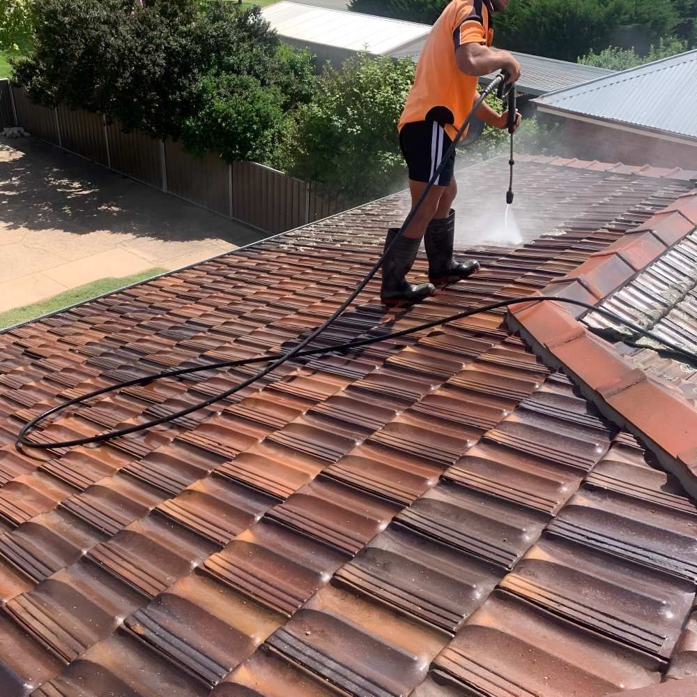 A Man Is Cleaning A Tiled Roof With A High Pressure Washer — Lance Ward Roof Tiling in Orange, NSW