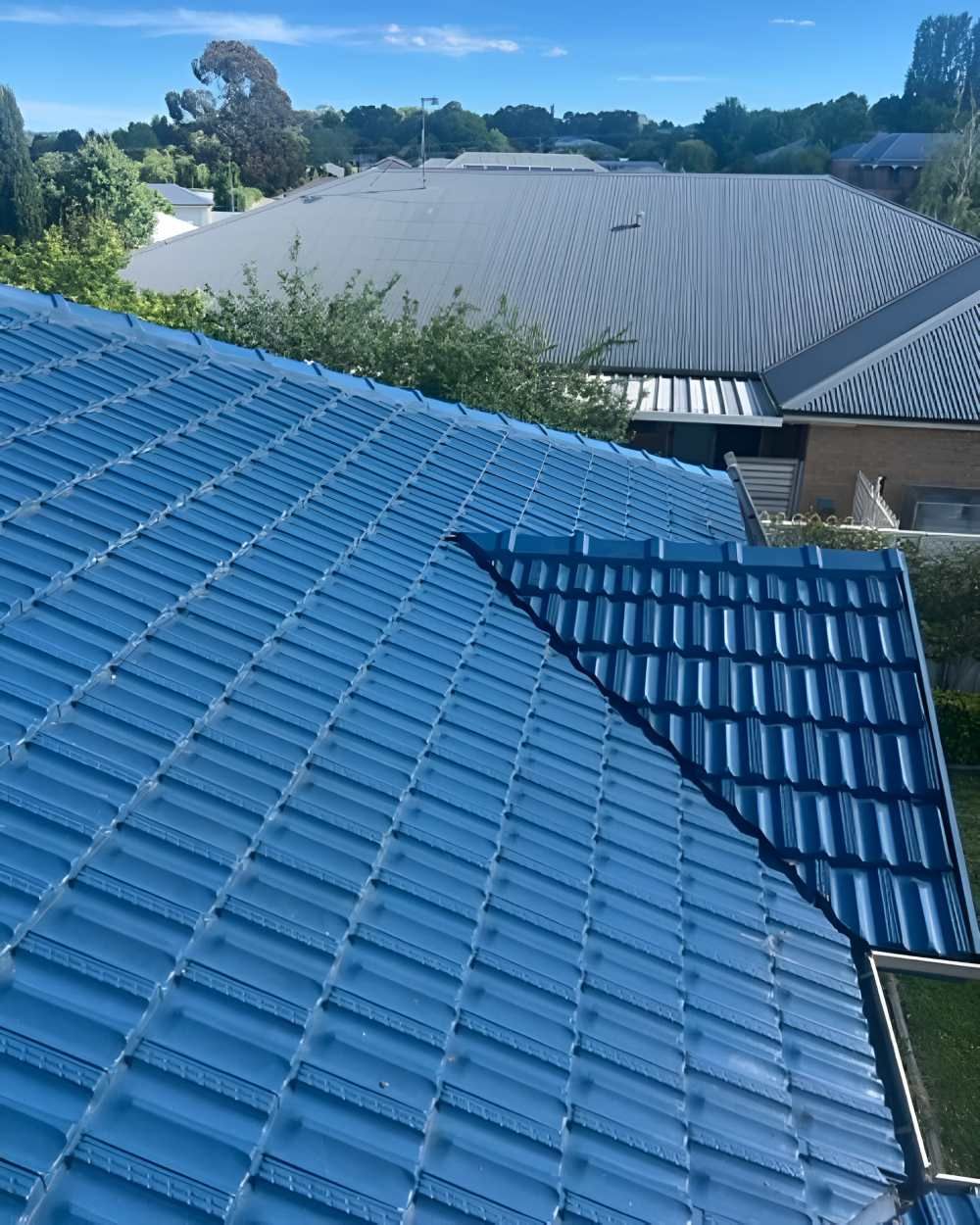 A Blue Tiled Roof Of A House With Trees In The Background — Lance Ward Roof Tiling in Orange, NSW