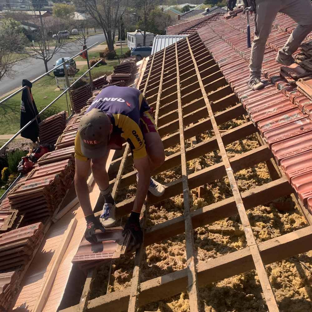 A Man Is Working And Repairing The Roof Of A House — Lance Ward Roof Tiling in Orange, NSW