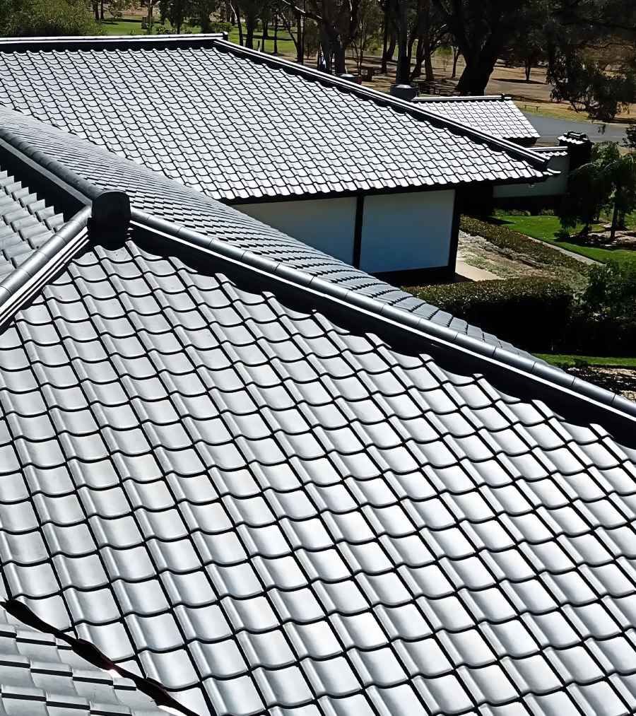 A Black Tiled Roof With A White Building In The Background — Lance Ward Roof Tiling in Cowra, NSW