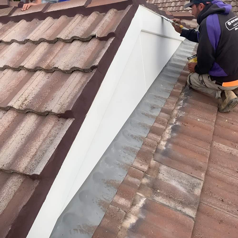 A Man Is Kneeling On A Roof With A Tape Measure — Lance Ward Roof Tiling in Cowra, NSW