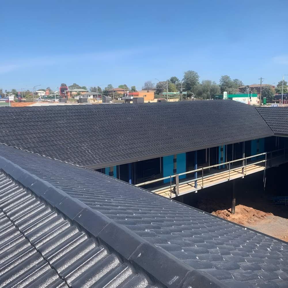 A Large Building With A Black Roof Is Under Construction — Lance Ward Roof Tiling in Parkes, NSW