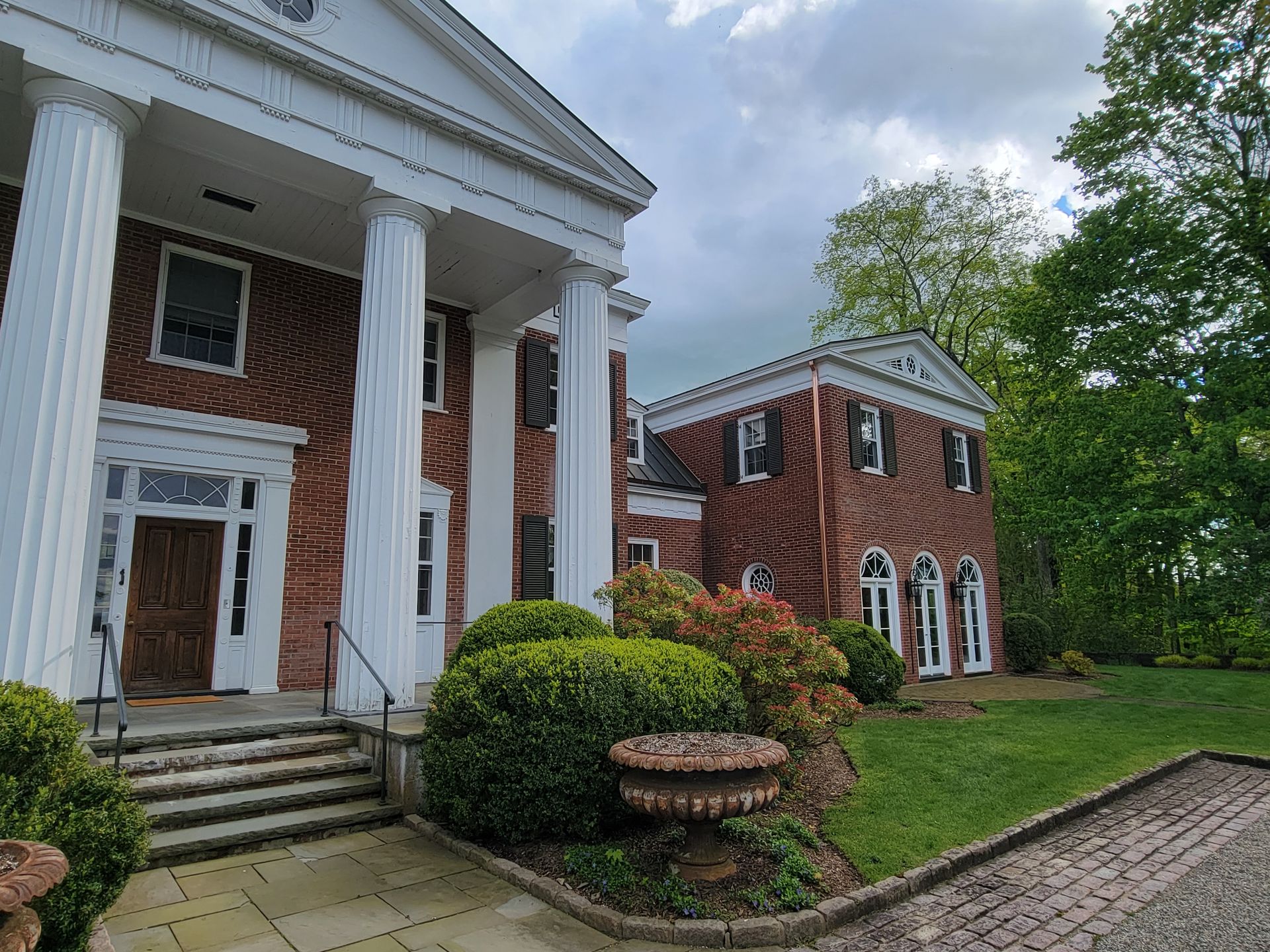 A large brick building with white columns is surrounded by trees and bushes.