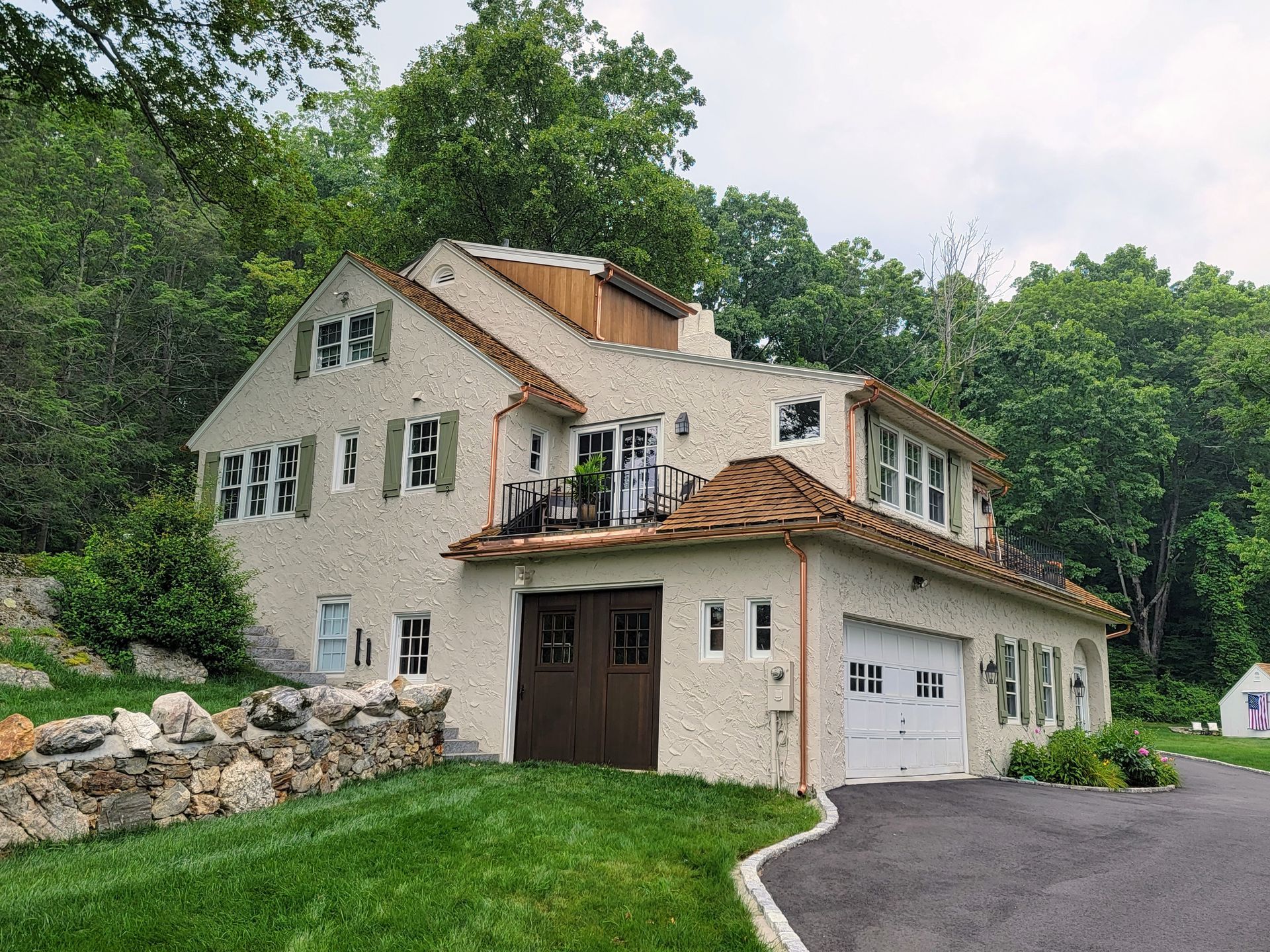 A large house with a garage and a balcony is surrounded by trees.