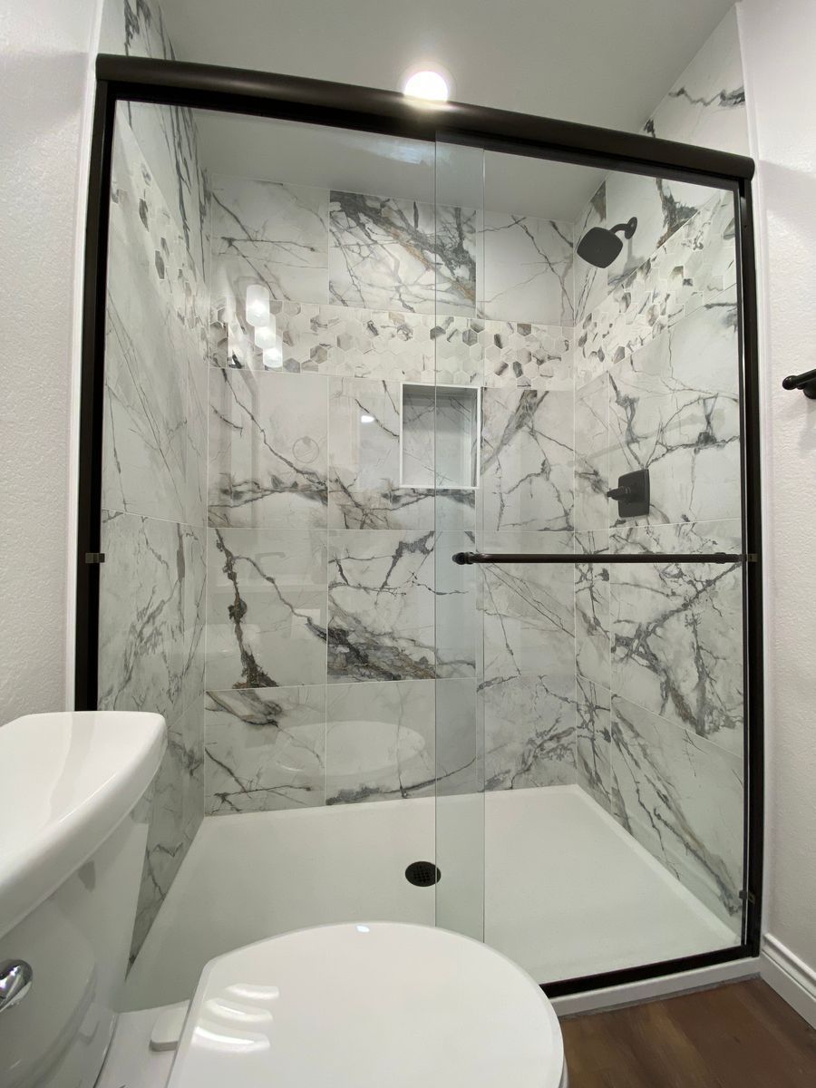 A bathroom with a toilet , shower and marble walls.