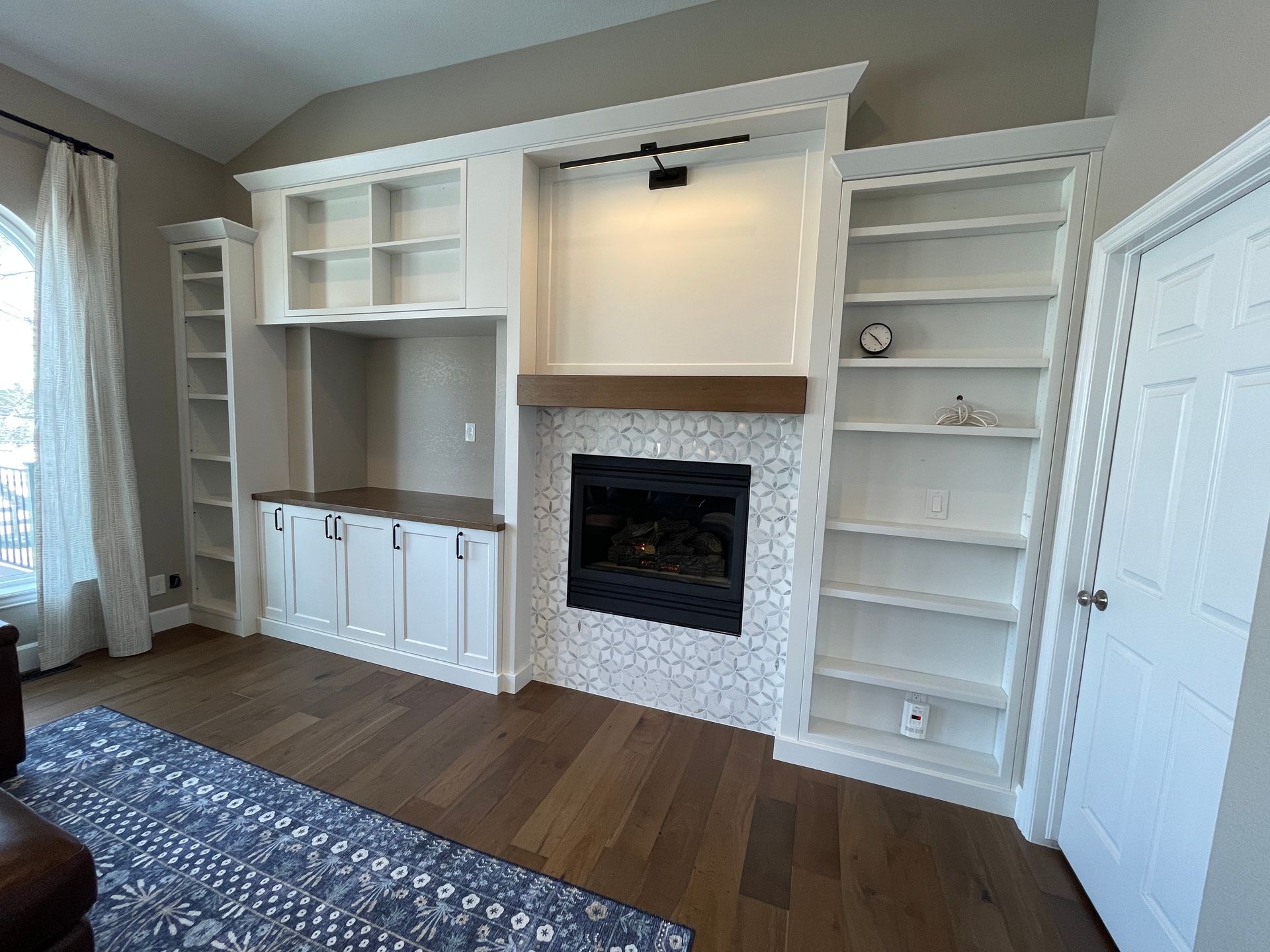 A living room with a fireplace , shelves , cabinets and a rug.