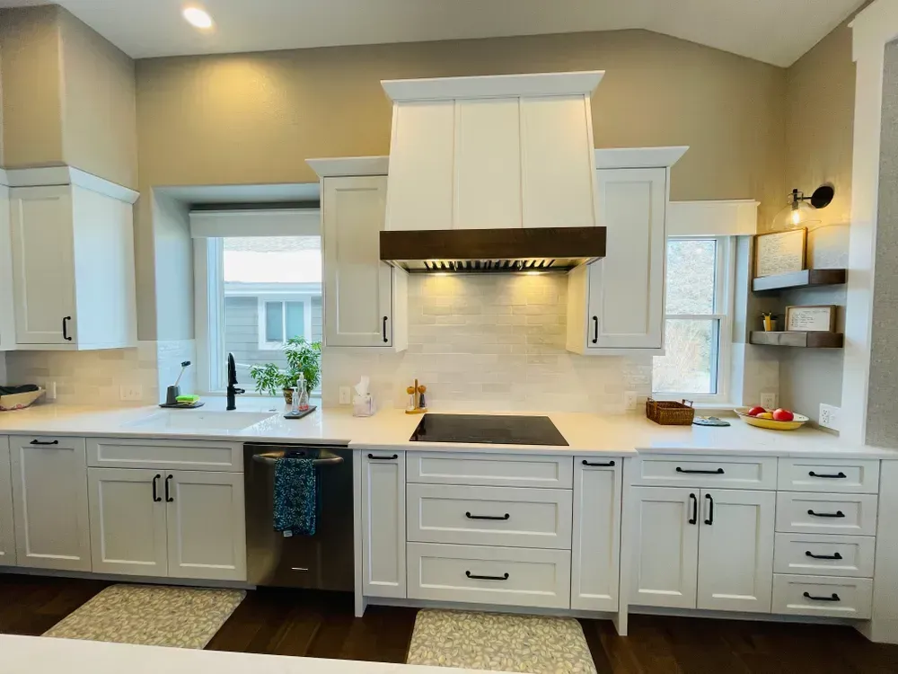 A kitchen with white cabinets , a stove , a sink , and a window.