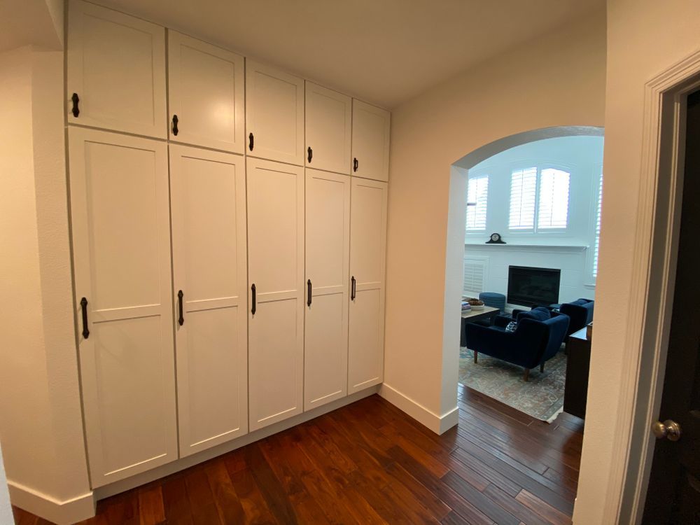 A hallway with white cabinets and hardwood floors leading to a living room.